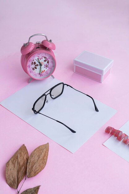 Presentazione del prodotto del concetto minimalista idea occhiali quadrati regalo orologio e foglie secche su sfondo di carta rosa