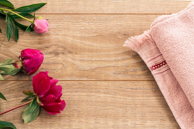 Producten voor gezichts- en lichaamsverzorging. Zachte badstof handdoek en pioenroos bloemen op de houten achtergrond. Spa- en lichaamsverzorgingsset. Bovenaanzicht.