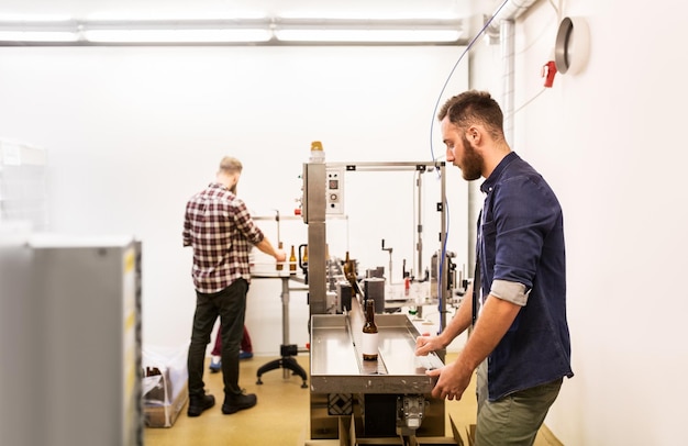 productie-, bedrijfs- en mensenconcept - mannen met flessen op transportband bij ambachtelijke brouwerij of bierfabriek