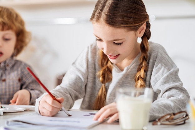 Productief en geïnspireerd. Gemotiveerde artistieke opgetogen dame die 's ochtends tekent met aquarellen en probeert haar huiswerk tijdens het weekend af te maken