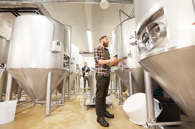 Foto concetto di produzione, attività e persone - uomini con schede che lavorano in un birrificio artigianale o in un impianto di birra analcolica