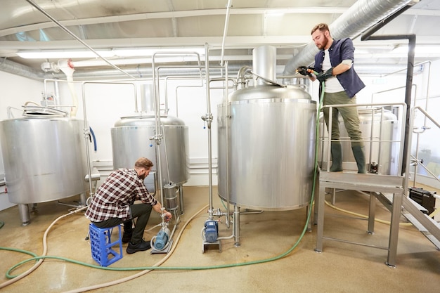 Photo production, business and people concept - men working with kettles and compressors at craft beer brewery or non-alcoholic beverage plant