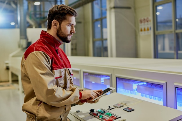 Production line operator working on digital tablet while supervising woodworking automated machine