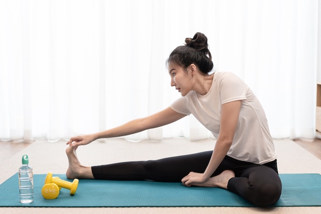 Productive activity concept a girl stretching her body by touching the hand with the toes beside the pair of yellow dumbbells and a fresh water.