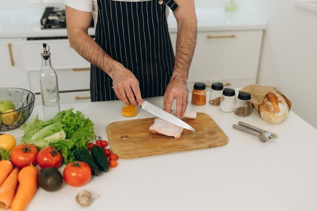 Products for cooking on the kitchen table A man cuts a chicken on a board