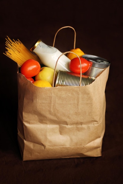 Products in a paper bag on a brown linen background. Food in a food delivery service package. Canned food, pasta, vegetables, fruits, milk. Contactless delivery.