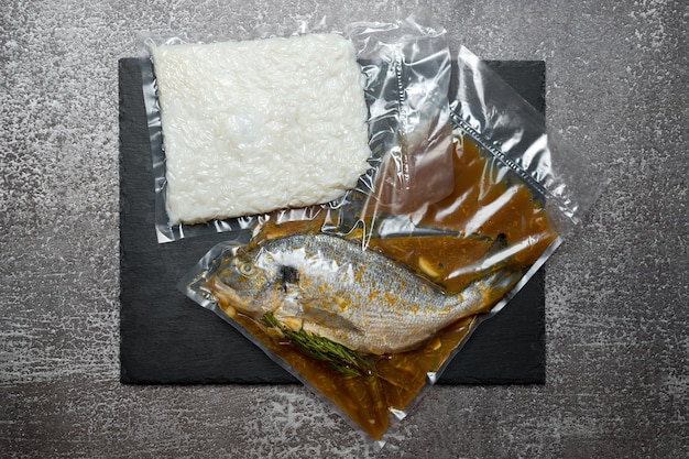 Products in vacuum packaging on black slate board. Fish and rice, vacuum sealed food ready for sous vide cooking. Sous-vide, new technology cuisine, new normal in quarantine pandemic time.