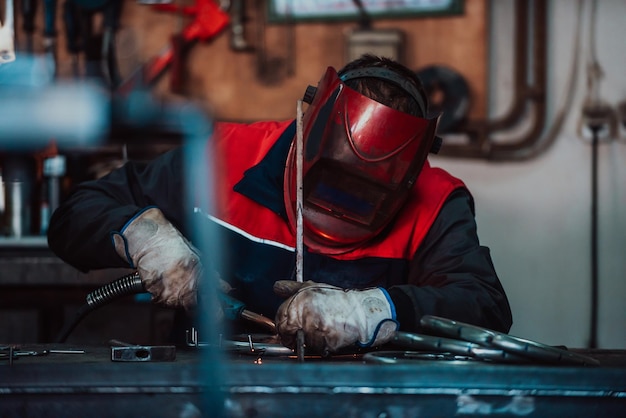 Profesional welder in protective uniform and mask welding metal pipe on the industrial table with ot