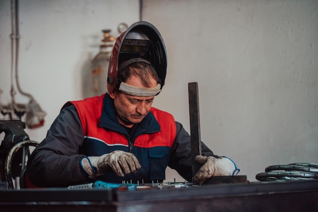 Profesional welder in protective uniform and mask welding metal pipe on the industrial table with ot