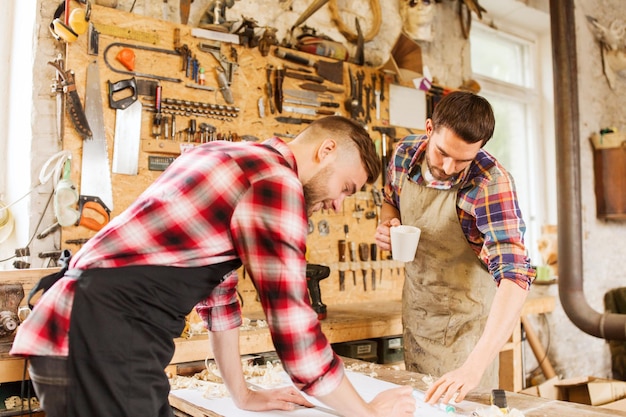 profession, carpentry, woodwork and people concept - two carpenters with ruler and blueprint at workshop