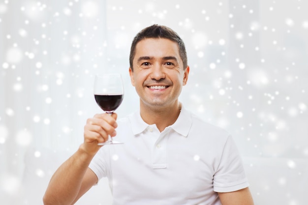 концепция профессии, напитков, досуга, праздников и людей - счастливый человек пьет красное вино из бокала дома над эффектом снега
