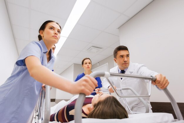 profession, people, health care, reanimation and medicine concept - group of medics or doctors carrying unconscious woman patient on hospital gurney to emergency