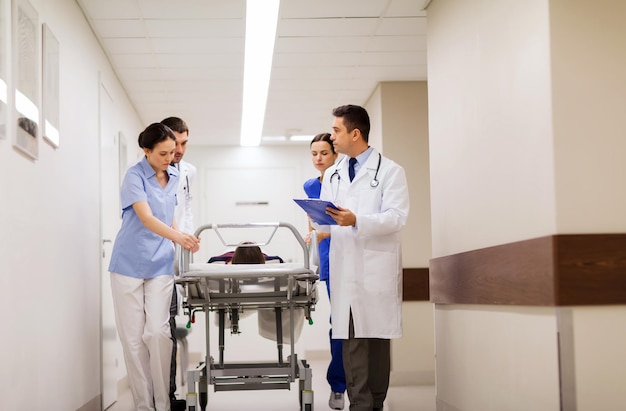 profession, people, health care, reanimation and medicine concept - group of medics or doctors carrying unconscious woman patient on hospital gurney to emergency