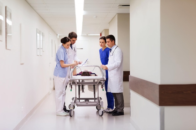 profession, people, health care, reanimation and medicine concept - group of medics or doctors carrying unconscious woman patient on hospital gurney to emergency