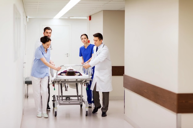 profession, people, health care, reanimation and medicine concept - group of medics or doctors carrying unconscious woman patient on hospital gurney to emergency