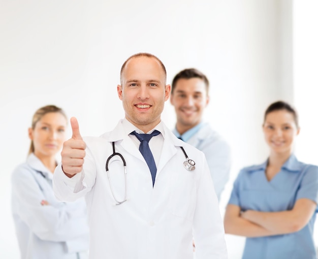 profession, teamwork, gesture and medicine concept - smiling male doctor with stethoscope in coat over group of medics showing thumbs up