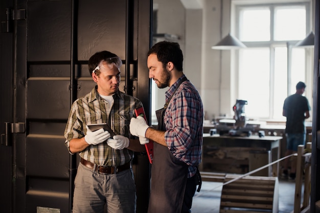 Profession, technology and people concept - two workmen with tablet pc computer at workshop