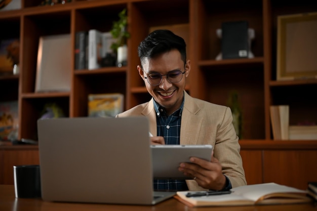 Uomo d'affari asiatico adulto professionista che utilizza il suo tablet per gestire i suoi compiti alla sua scrivania