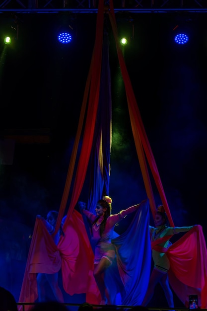 Professional aerialist circus performer on red bright aerial silks performs balance on a splits