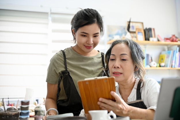 Professional aged woman showing the moulding clay instruction\
on the paper to young female