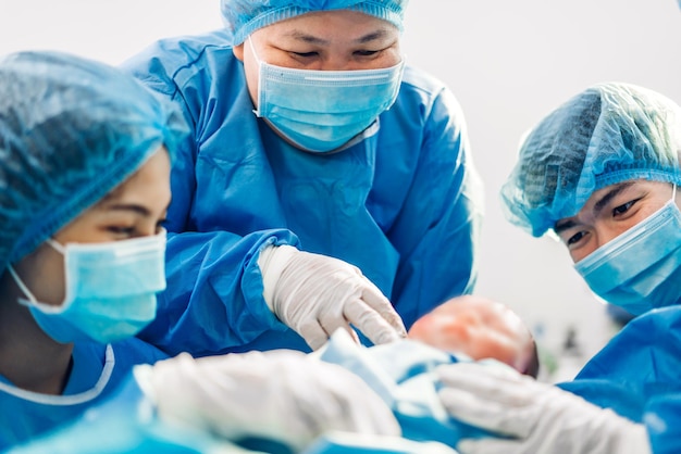 専門の麻酔科医の医師の医療チームとアシスタントが赤ちゃんの帝王切開を行い、現代の病院の手術室で手術器具を使って出産する赤ちゃんを抱きしめています