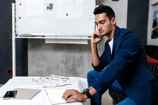 Professional architect dressed in stylish clothes makes notes in a notebook on a table with a drawing ruler and phone .