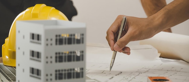 Foto ingegnere professionista dell'architetto o revisione della mano interna del progetto con il modello dell'edificio sulla scrivania del posto di lavoro nel centro dell'ufficio al concetto di ingegneria edile dell'appaltatore del cantiere