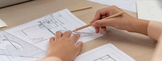 Professional architect hand drawing a blueprint by using ruler measuring length on table with architectural equipment and blue print scatter around at modern office Closeup Delineation