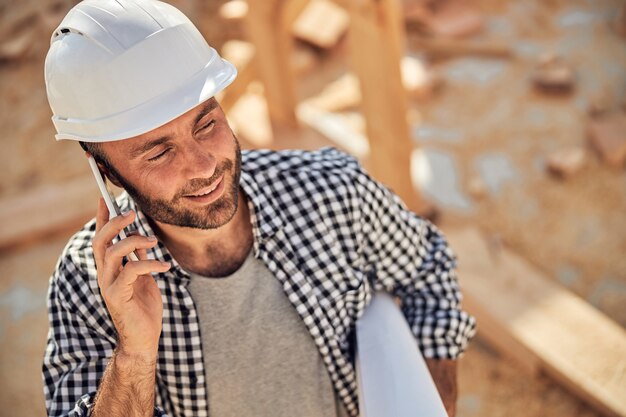 Architetto professionista che fa una telefonata e tiene in mano un rotolo di carta