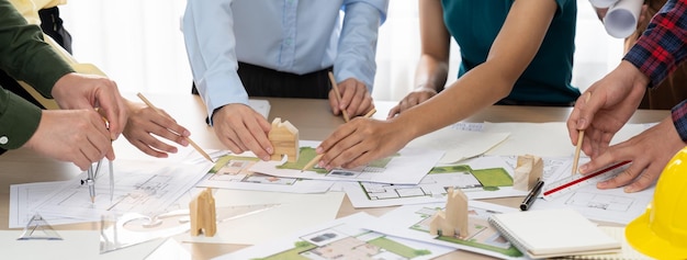 전문 건축가 팀은 생활 및 디자인 개념 주변에 흩어져 있는 녹색 디자인 문서와 건축 장비를 사용하여 회의 테이블에 에코 하우스를 지을 계획입니다.