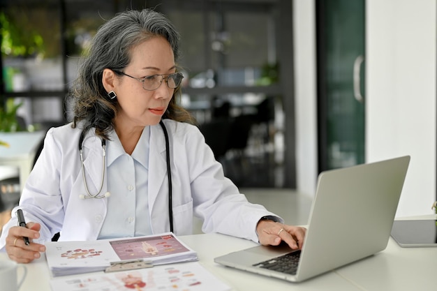 Professional Asian aged female doctor concentrating working on her medical research using laptop