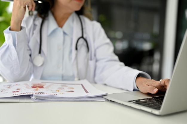 Foto medico femminile invecchiato asiatico professionista che utilizza il computer portatile che lavora alla sua scrivania nell'ufficio del medico