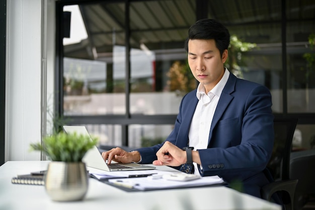 Professional Asian businessman checking time on his wristwatch while working at his desk