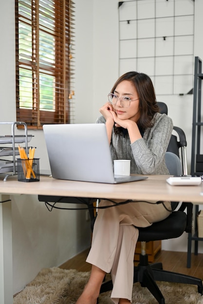 노트북 화면을 보며 숙고하는 그녀의 작업에 집중하는 전문 아시아 여성