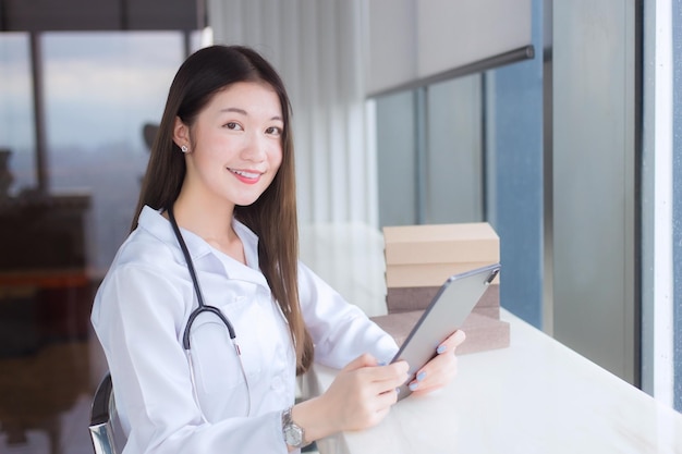 Professional Asian female doctor dressed in white medical coat sits on chair at a hospital library