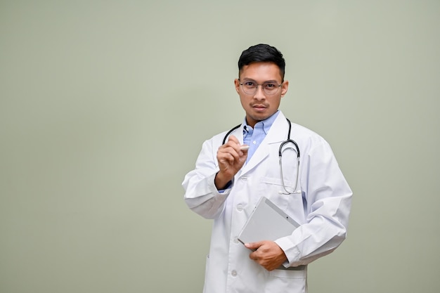 Photo professional asian male doctor pointing pen at the camera standing against green background