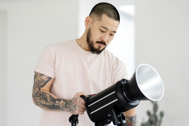 Professional asian photographer with stylish tattoos setting up lighting in modern studio