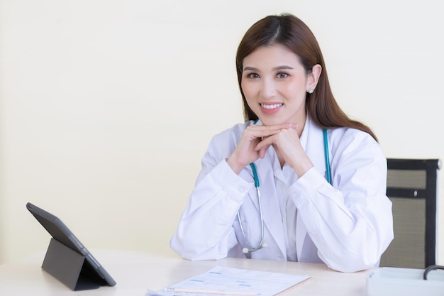 Foto professionale giovane dottoressa sorridente asiatica seduta in ufficio in ospedale sul tavolo ha tablet.