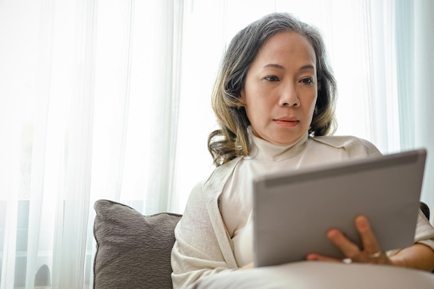 A professional Asianaged businesswoman managing business tasks on a digital tablet