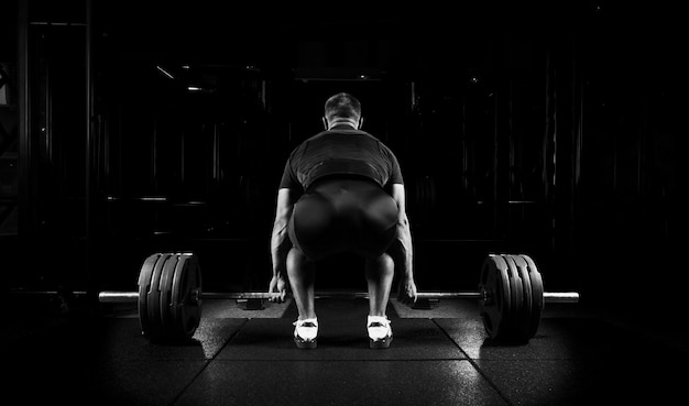 Professional athlete sits in front of the bar and is preparing to raise it. Back view