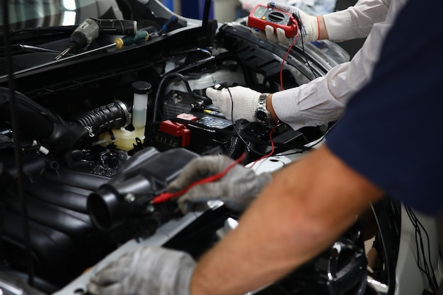 Professional auto mechanic works in a car service and tests operation of engine with tester