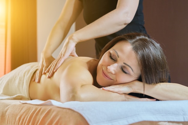 Процедура профессионального массажа спины, взрослая женщина, получающая лечение, лежа на массажном столе