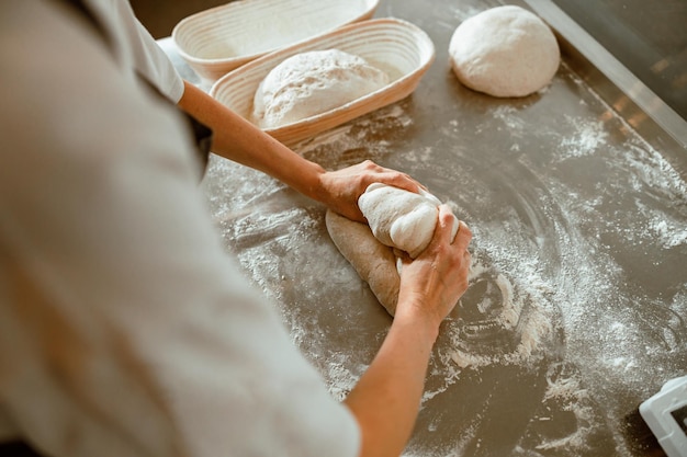 Professional baker kneads raw dough to make delicious bread in workshop