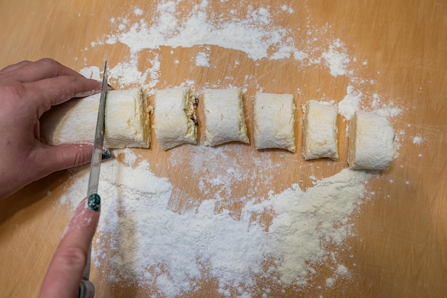 Professional baker with knife cuts the raw sausage dough into even small pieces making cheese cakes a Ukrainian national dish