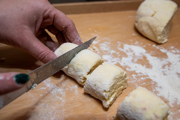 Professional baker with knife cuts the raw sausage dough into even small pieces