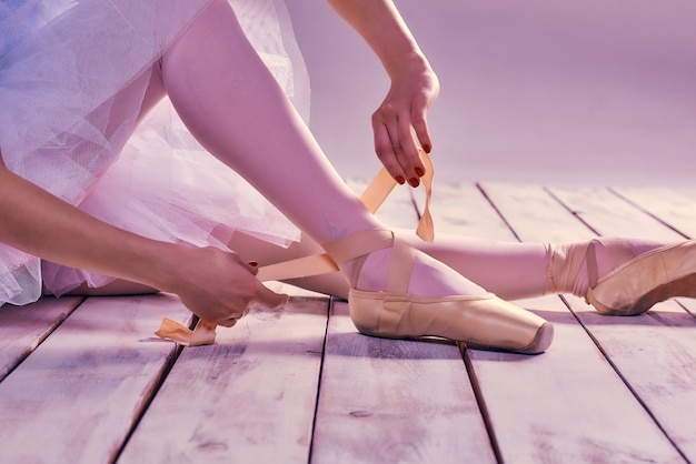 Ballerina professionista che indossa le sue scarpe da ballo sul pavimento di legno su uno sfondo rosa. primo piano dei piedi