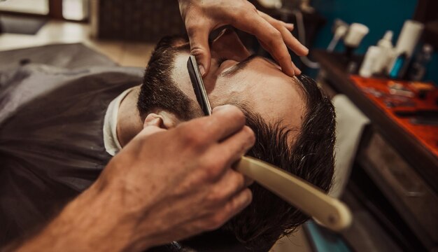 A professional barber cuts his beard to a young hipster man