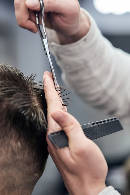 Профессиональный парикмахер делает стрижку молодому человеку с помощью ножниц и расчески в парикмахерской