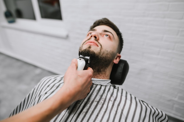 Professional barber with a hair clipper in his hand makes a beard hairstyle for the client