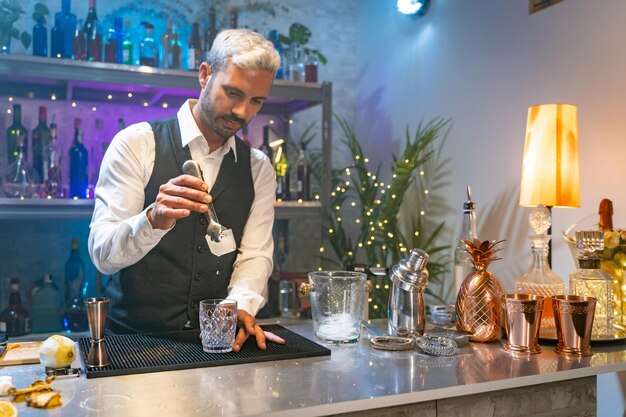 Barman professionista in camicia bianca e grembiule nero che prepara cocktail alla festa in discoteca quasi vita